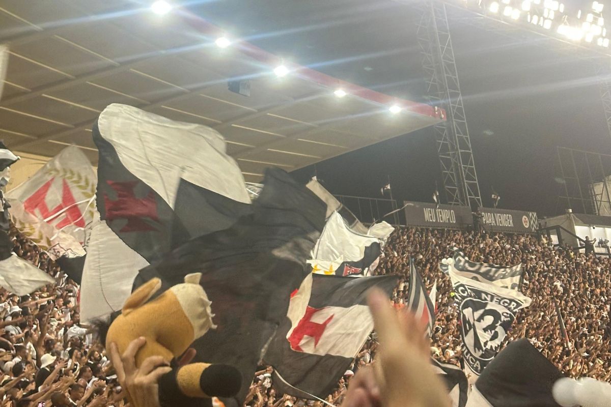 Torcida do Vasco agitando bandeiras alvinegras com a cruz de malta na arquibancada de São Januário à noite