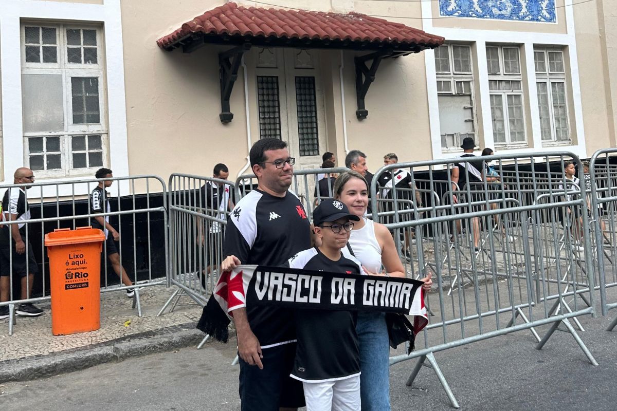 Família de torcedores do Vasco segurando cachecol Vasco da Gama em frente à fachada histórica de São Januário
