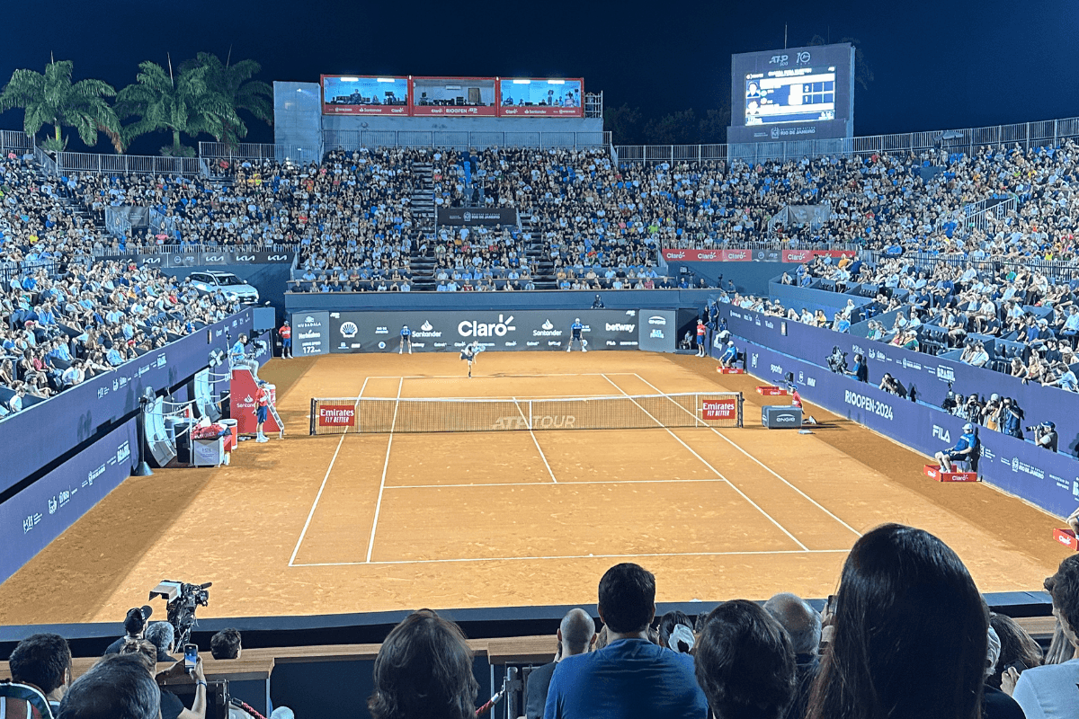 Partida noturna de tênis no Rio Open, quadra de saibro com arquibancadas lotadas no Jockey Club Brasileiro